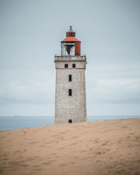 Lighthouse on beach by sea against sky