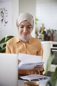 Smiling woman with hijab checking bills at home