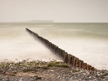 Wooden posts in sea against clear sky