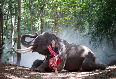 Woman sitting by elephant in forest