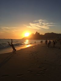 Silhouette people on beach against sky during sunset