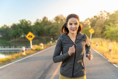 Happy attractive young woman wearing her warm up jacket while running at a local park