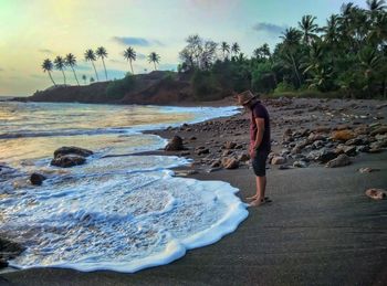 Man standing on rock at beach against sky