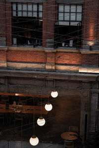 Low angle view of illuminated light bulbs hanging against building