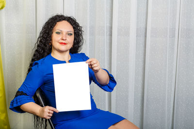 Portrait of a beautiful young woman sitting against blue wall