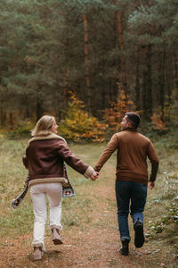 Adult couple having fun together in autumn park, man and woman are holding hands while running