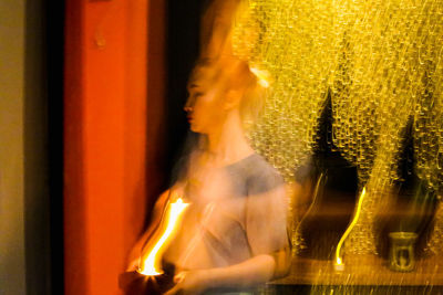 Portrait of woman looking at illuminated window