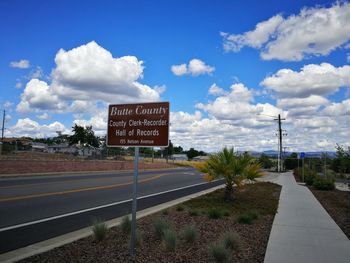 Road sign by street against sky in city