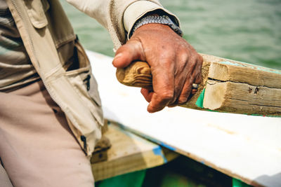 Midsection of man holding wooden oar in boat on sea