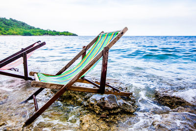 Abandoned deck chairs at beach against sky