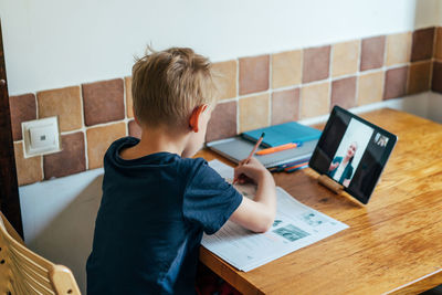 Rear view of boy using mobile phone while sitting on table