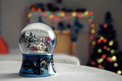 Close-up of snow globe on table with christmas tree in background