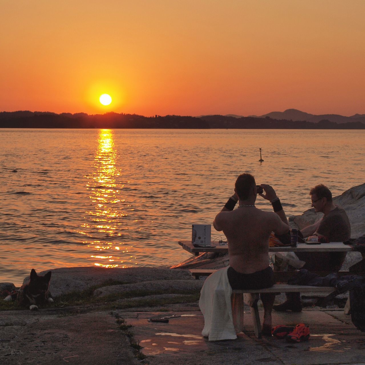 sunset, water, sun, orange color, leisure activity, lifestyles, silhouette, sitting, scenics, beauty in nature, men, tranquil scene, tranquility, person, nature, sky, sea