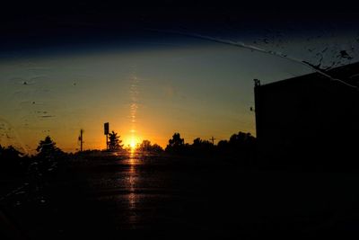 Silhouette buildings by trees against sky during sunset