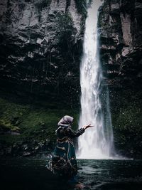 Full length of woman standing against waterfall in forest