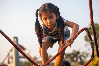 Portrait of cute girl holding rope at playground against clear sky