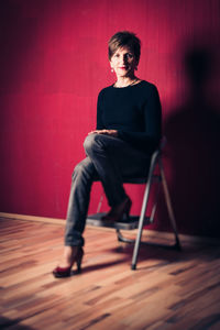Full length of young woman sitting on chair against wall