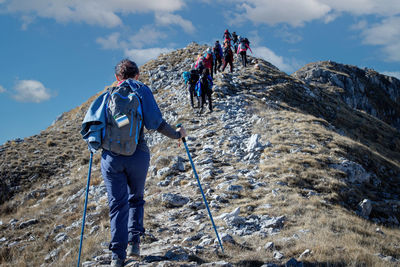 Group of hikers walk on the mountain path, helping themselves up the climb with trekking poles.