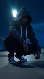 Rear view of man sitting on illuminated street at night