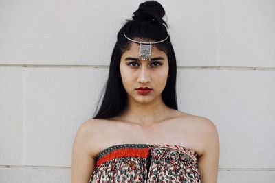 Portrait of young woman standing against wall