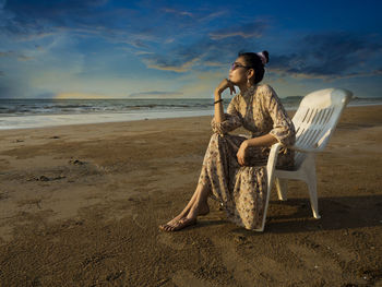 Woman sitting on beach by sea against sky