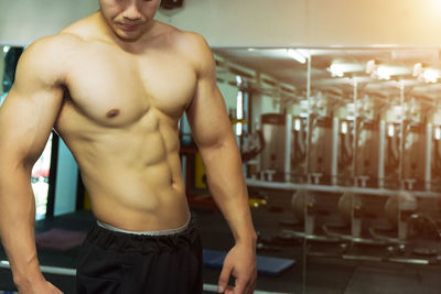 Midsection of shirtless muscular man exercising at gym