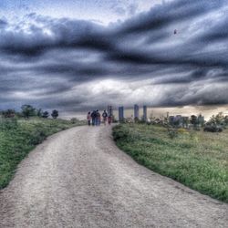 Road passing through field against cloudy sky