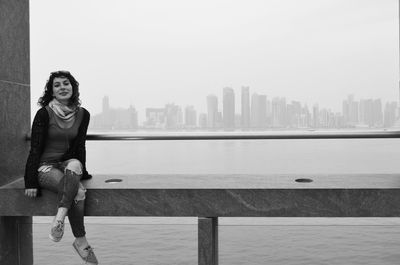 Full length portrait of man sitting in city against clear sky