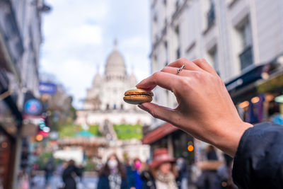 Hand holding a french macaroon cookie, macaron, on the street of paris