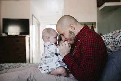 Side view of father playing with daughter while sitting on bed at home