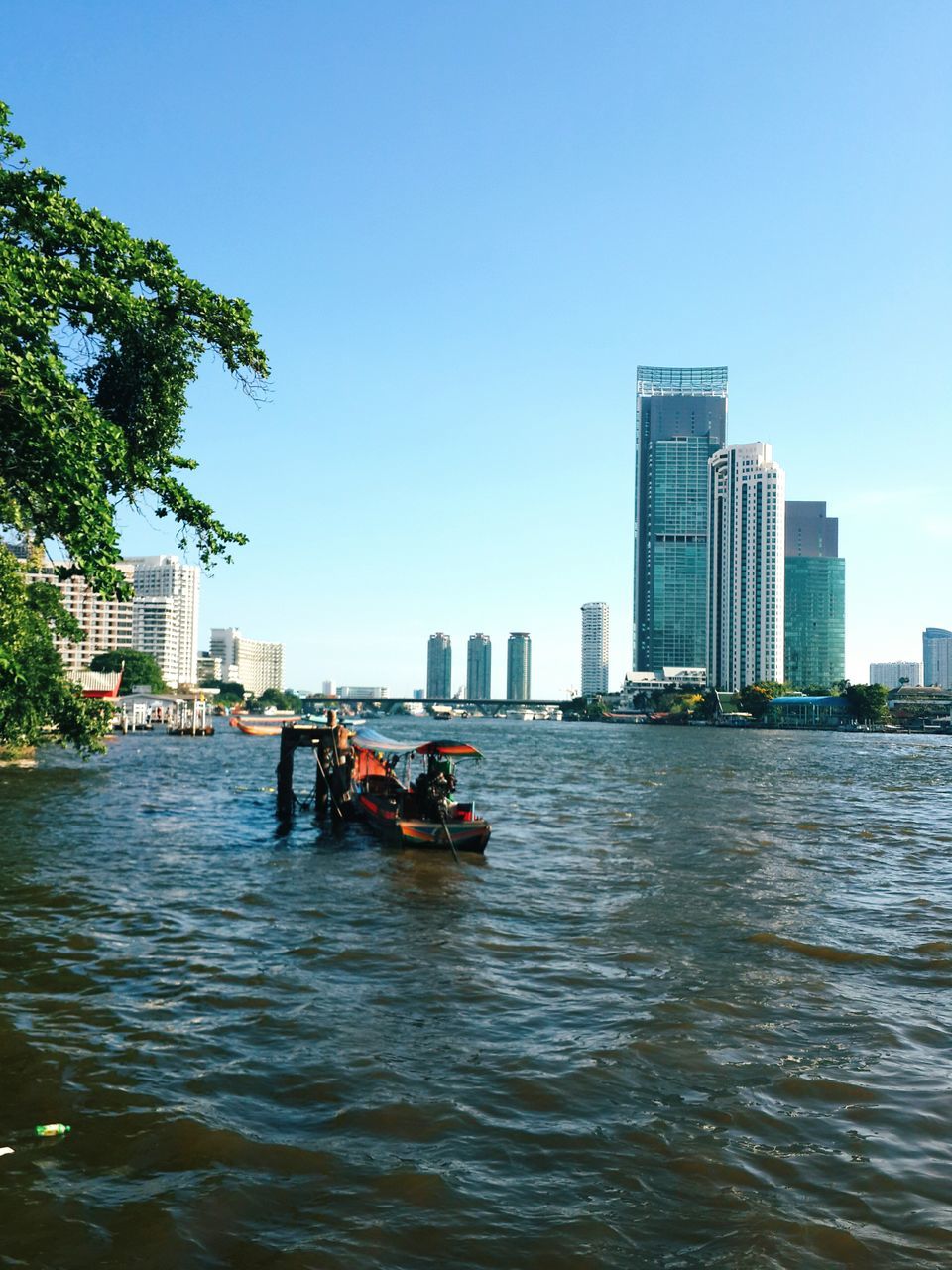 building exterior, architecture, city, water, clear sky, built structure, waterfront, skyscraper, cityscape, river, urban skyline, copy space, nautical vessel, blue, tall - high, office building, transportation, tower, modern, tree