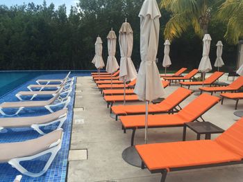 Lounge chairs by closed parasols by swimming pool