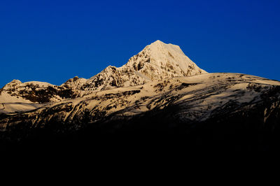 Low angle view of snowcapped mountain against clear blue sky