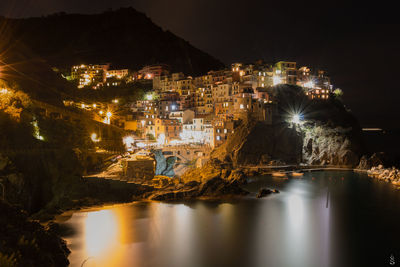 Illuminated town by calm sea at night