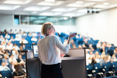 Female speaker giving a talk on corporate business conference. unrecognizable people in audience at