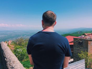 Rear view of man looking at view while standing on retaining wall