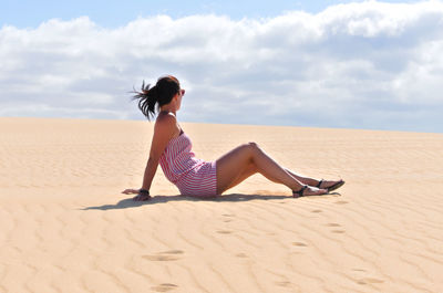 Full length of woman sitting on sand at desert against sky
