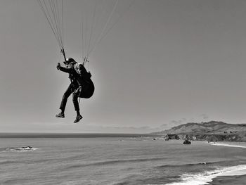 Man paragliding over the ocean against cliffs.