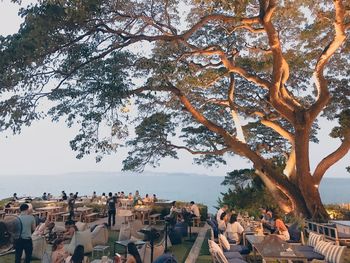 Group of people on tree trunk by sea against sky