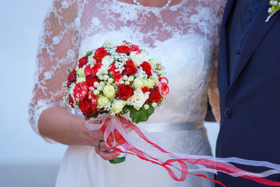 Midsection of woman holding bouquet against red wall