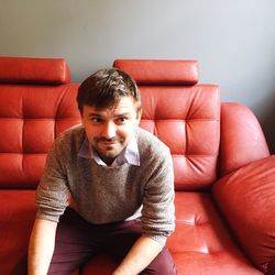 Man looking away while relaxing on red sofa at home