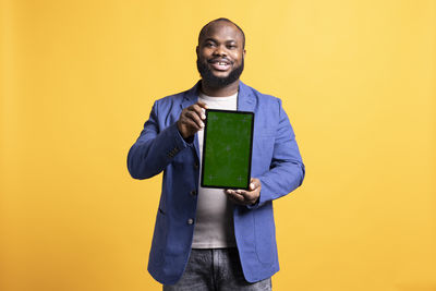 Portrait of smiling young man standing against yellow background