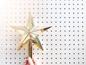 Cropped hand holding star shaped christmas ornament against wall
