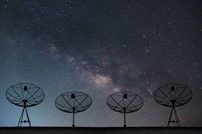 Low angle view of satellite dishes against star field sky at night
