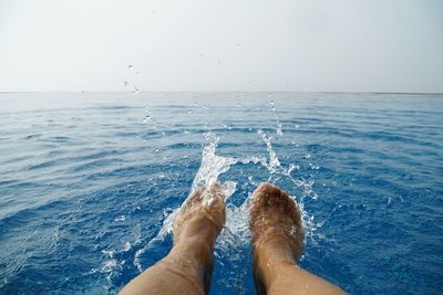 Low section of person in infinity pool against clear sky