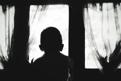 Rear view of silhouette man standing against window