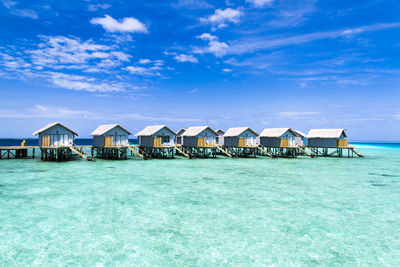 Stilt houses by sea against blue sky