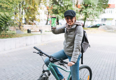 Portrait of young pretty woman in cap and sunglasses using mobile on bicycle on sunny autumn day 