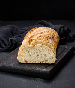 Baked whole oval bread made from white wheat flour on a black table, fresh pastries