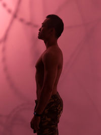 Side view of shirtless man standing against pink wall